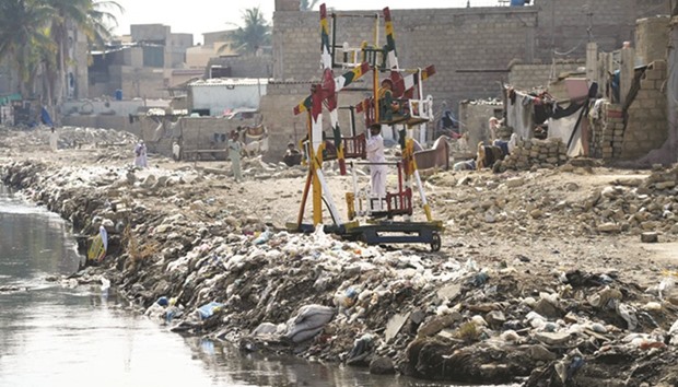 Children ride on swings alongside dumped garbage in Karachi.