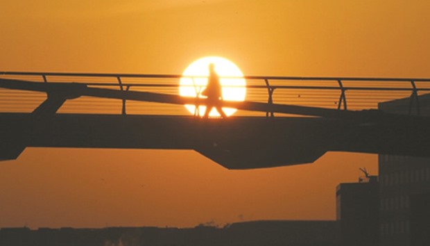 An early commuter is silhouetted by the rising sun on the Millennium Bridge across the Thames.