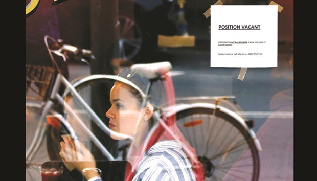 Customers at a local cafe are seen through a window displaying a job vacancy notice in central Sydney, Australia.