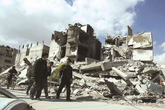 Syrians walk amid the rubble of buildings which were destroyed earlier in regime air strikes, in the rebel-held besieged town of Douma in the eastern Ghouta region, on the outskirts of the capital Damascus, yesterday.