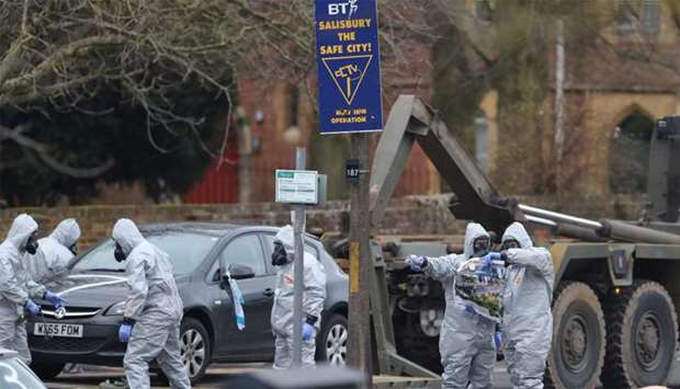Military personnel wearing protective coveralls look at a map while others load a car onto a military vehicle in a cordoned off area behind a police station in Salisbury