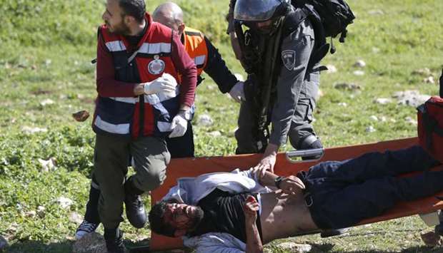 An Israeli soldier attempts to detain an injured Palestinian demonstrator as he's carried on a stretcher by Palestinian Civil Defence volunteers on March 12, 2018 in the West Bank town of Birzeit, near Ramallah, during a protest by students of the Birzeit University against the arrest of the the head of Palestinian student council by an Israeli undercover commando.