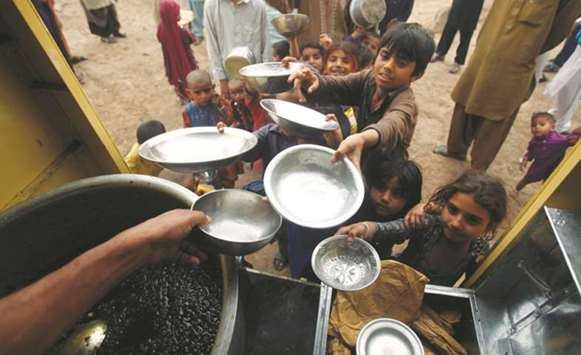 Children hold out their bowls as they wait yesterday during a charity food handout in Peshawar.