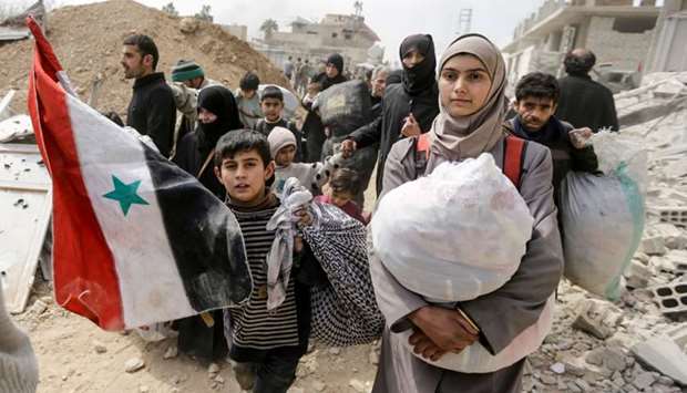 A Syrian child walks with a national flag with other civilians evacuated from the Eastern Ghouta enclave, as they pass with belongings through the regime-controlled corridor opened by government forces in Hawsh al-Ashaari, east of the enclave town of Hamouria on the outskirts of the capital Damascus.