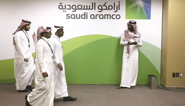 Attendees walk by a sign for Aramco on display inside the King Abdulaziz Center for World Culture during a tour of the project in Dhahran on November 25, 2016. US investors have reportedly pushed back at several aspects of the Aramco IPO plan, with issues raised including the $2tn valuation Saudi Arabia wants for the worldu2019s largest oil producer, the scale of dividends Aramcou2019s prepared to pay and the impact of the shale boom on oil prices over the next few years.