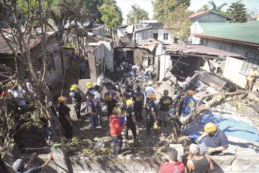 Rescuers and investigators stand at the site where a twin-engined plane crashed into a house just after taking off in Plaridel town, Bulacan province, north of Manila, yesterday.