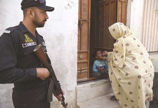 A health worker administers polio vaccine drops to a child as a policeman stands guard during a polio campaign in Karachi.