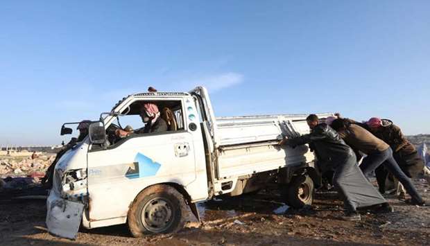 Displaced Syrians push a damaged vehicle following a reported air strike on a refugee camp near the northwestern town of Hass, in Idlib province