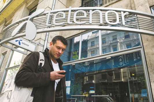 A pedestrian checks his mobile handset while passing a Telenor mobile phone store in Budapest. The sale includes Telenoru2019s mobile operations in Hungary, Bulgaria, Montenegro and Serbia and the technology service provider Telenor Common Operation.