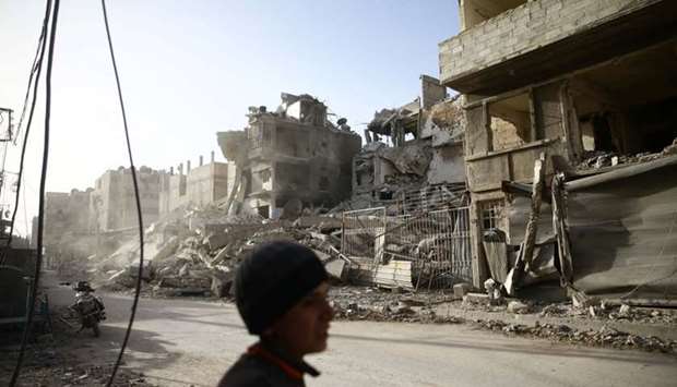 A boy walks near damaged buildings in the besieged town of Douma in eastern Ghouta in Damascus, Syria