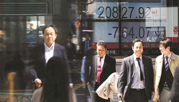 People walk past an electronic board showing stock prices outside a brokerage in Tokyo. The Nikkei 225 closed down 4.5% to 20,617.86 points yesterday.