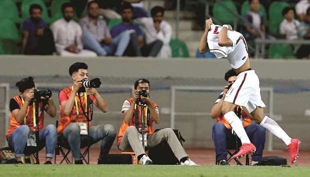 Akram Afif takes off his shirt to celebrate his goal against Syria. At right, fans cheer as they display the Qatari flag.