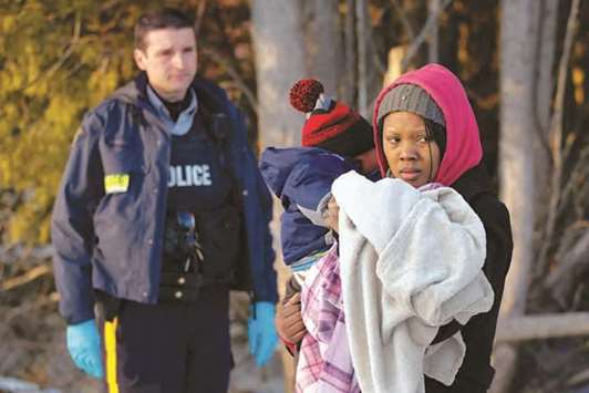 A Royal Canadian Mounted Police officer looks on as a woman carrying a child waits to cross the US-Canada border into Canada in Champlain, New York.
