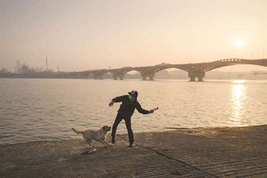 A man throws a bottle for his dog before the Han river in Seoul yesterday. South Korea is bracing for days of poor air quality as rising seasonal temperatures and an unfavourable wind direction threatens to compound local pollution, resulting in government issued u2018fine dustu2019 warnings with air quality monitoring websites reporting PM 2.5 levels of over 200, or u2018unhealthyu2019 u2013 eight times higher than the guideline limit for 24-hour exposure advised by the World Health Organisation (WHO).