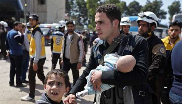 A Syrian evacuee from Eastern Ghouta carries an infant after arriving with others in the village of Qalaat al-Madiq on Tuesday.