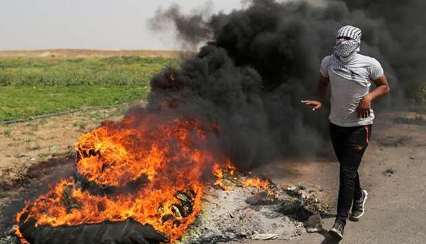 A Palestinian runs next to burning tyres during clashes along the Israel border with Gaza ahead of a protest in a tent city, demanding to return to their homeland, in the southern Gaza Strip yesterday. Reuters