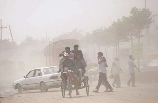 People move around in a street as dust envelopes Dhaka.