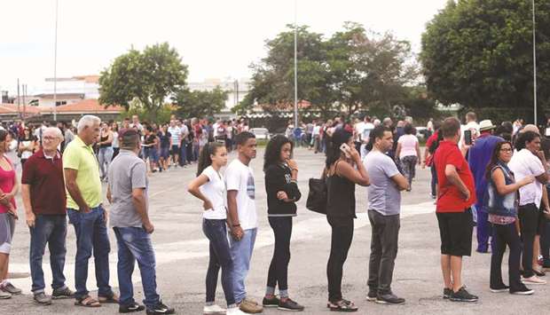 People stand outside Arena Suzano where family, friends and students attend the collective funeral of the victims killed in a shooting at Raul Brasil School in Suzano, Brazil, yesterday.