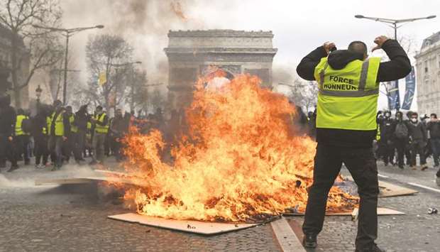 A u2018yellow vestu2019 protester gestures behind flames rising from a barricade in Paris yesterday.