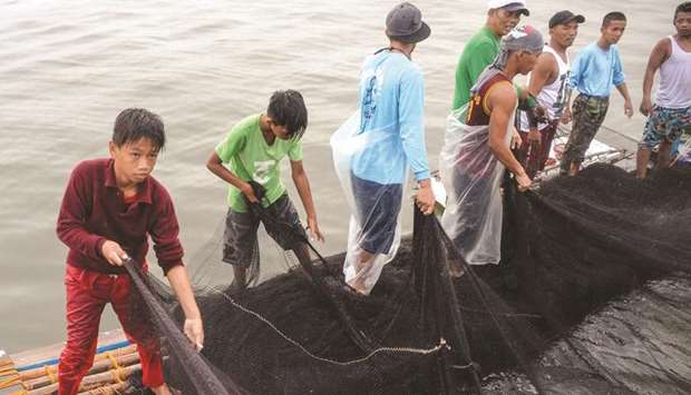 13-year-old Reymark Cavesirano (left) helps crew members with their nets onboard a fishing boat anchored at the mouth of Manila Bay off Navotas City in suburban Manila.
