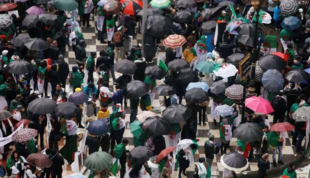 Demonstrators shield themselves from rain under umbrellas as they take part in a protest calling on President Abdelaziz Bouteflika to quit, in Algiers, Algeria