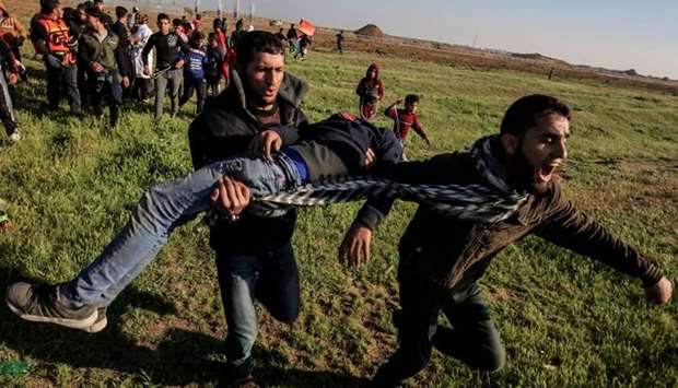 Palestinian men carry an injured protester at the border fence with Israel east of Gaza City on March 22. AFP