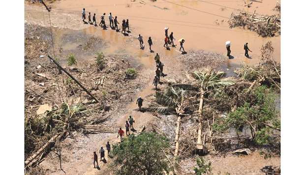 People walk past fallen palm trees as flood waters begin to recede in the aftermath of Cyclone Idai, in Buzi, near Beira, Mozambique, yesterday.