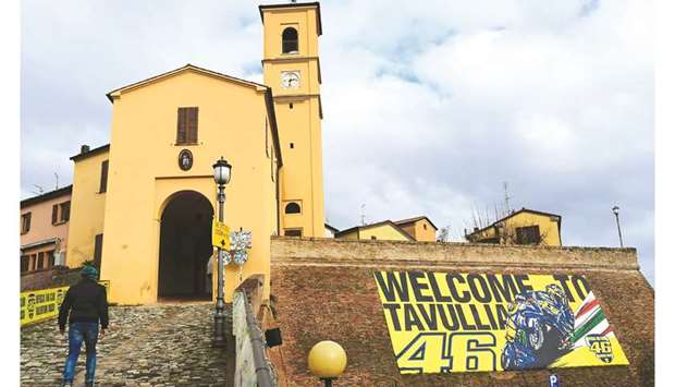 A welcome sign, featuring a drawing showing Italian motorcycle racer Valentino Rossi and his racing number 46, is pictured next to a church in Rossiu2019s hometown of Tavullia, on  January 29, 2019.  Everything in the Italian village reminds you that you are in Valentino Rossiu2019s hometown. The champion grew up here on the border of Marche and Emilia-Romagna in eastern Italy, and his racing number 46 is everywhere in Tavullia.