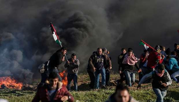 Palestinian protesters holding national flags walk past burning tyres during clashes with Israeli soldiers following a demonstration near the fence along the border with Israel, east of Gaza City.
