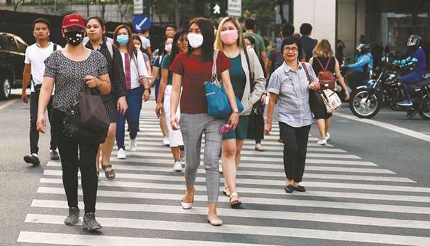 Pedestrians wear protective masks amid new cases of coronavirus in Manila, yesterday.