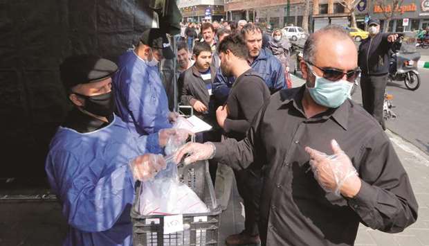 People queue in line to receive packages for precautions against Covid-19 coronavirus disease provided by the Basij militia, from a booth outside Meydane Valiasr metro station in the capital Tehran, yesterday.