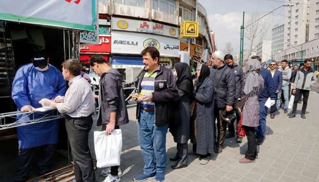 People queue in line to receive packages for precautions against coronavirus disease from a booth outside Meydane Valiasr metro station in the capital Tehran