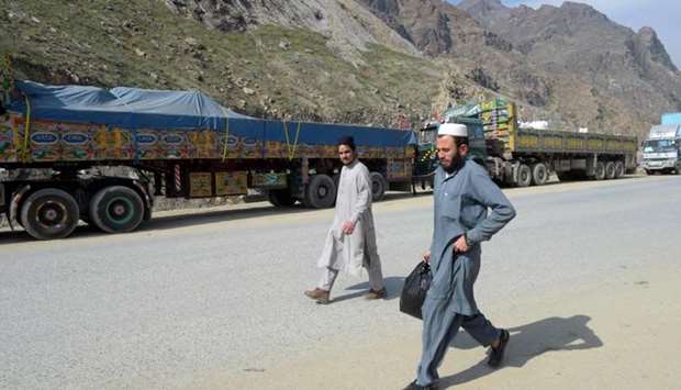 Men walk past Afghan's trucks parked along a road near the closed Pakistan-Afghanistan border amid concerns over the spread of the COVID-19 novel coronavirus, in Torkham