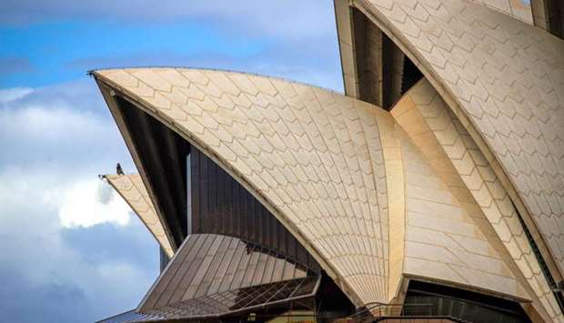 A worker (L) stands atop of the roof of the Sydney Opera House in Sydney on March 17, 2020. Management of the iconic building on March 17 announced the cancellation of all public performances until March 29
