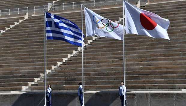 Athletes stand by the Greek, Olympic and Japanese flags during the olympic flame handover ceremony for the 2020 Tokyo Summer Olympics.