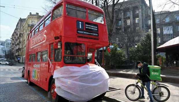 A deliveryman wearing a protective face mask pauses by a double-deck tourist bus decorated with a huge mask in the centre of the Ukrainian capital of Kyiv.