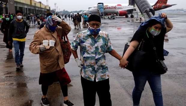 Travellers wearing protective masks and synthetic gloves walk on the tarmac to board an aircraft amid the spread of coronavirus disease (COVID-19) at Halim Perdanakusuma airport in Jakarta, Indonesia
