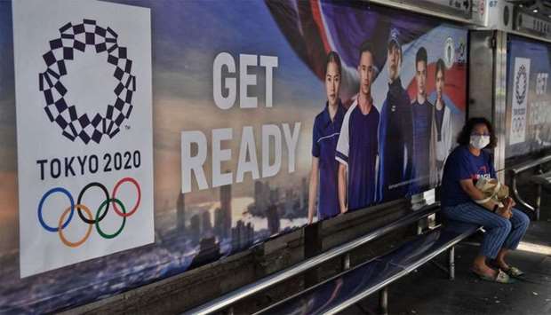 A woman wears a face mask amid concerns over the spread of the COVID-19 coronavirus as she sits at a bus stop advertising the Tokyo 2020 Summer Olympics