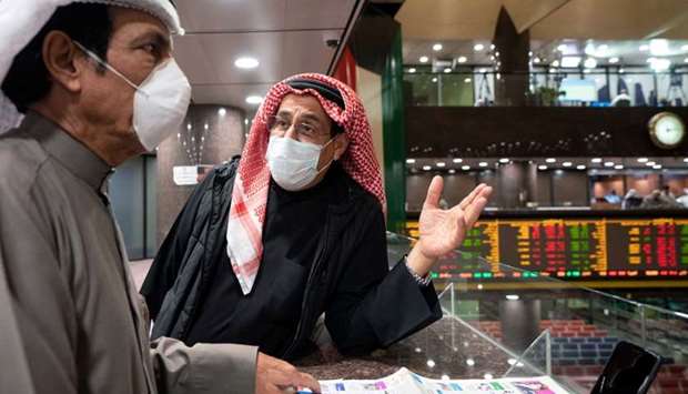 Kuwaiti traders wear protective face masks, following the outbreak of the new coronavirus, as they stand on the upper floor since the lower main hall is closed to traders at the Kuwait Boursa stock market trading in Kuwait city