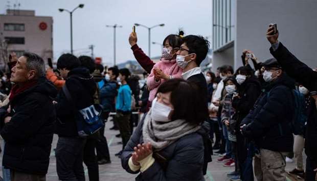 People wearing face masks watch the Tokyo 2020 Olympic flame displayed outside Miyako railway station, Iwate prefecture  after arriving from Greece