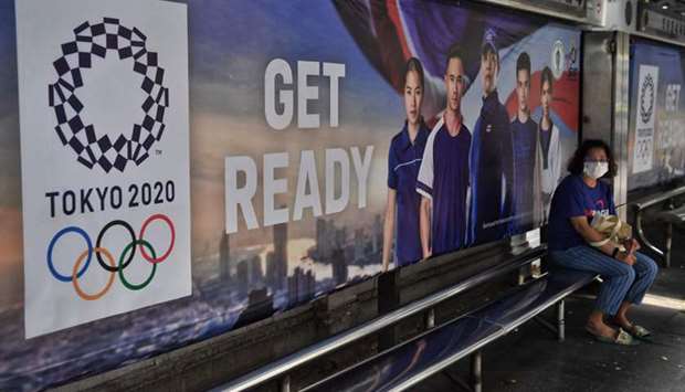 A woman wears a face mask amid concerns over the spread of the coronavirus as she sits at a bus stop advertising the Tokyo 2020 Summer Olympics in Bangkok on Friday. (AFP)