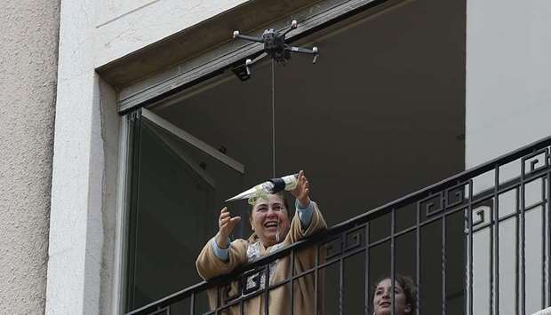 A woman standing on her balcony, reaches out to catch a rose delivered to her via a drone on Motheru2019s Day, in the Lebanese coastal city of Jounieh, north of the capital Beirut, yesterday, as people remain indoors in an effort to limit the spread of the novel coronavirus.