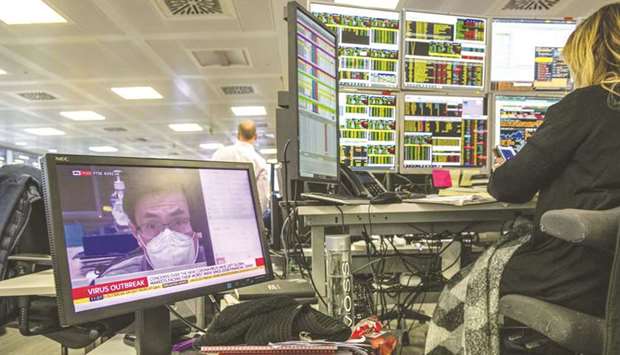 A television screen displays a news report about the coronavirus outbreak as a trader monitors financial data on computer screens on the trading floor at ETX Capital, a broker of contracts-for-difference, in London.