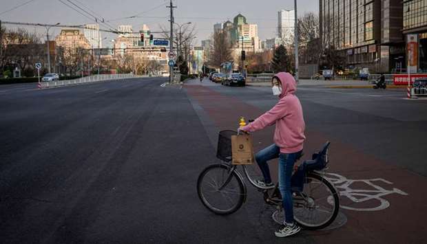 A woman wearing a face mask, as a preventive measure against the Covid-19 coronavirus, rides her bicycle on a nearly empty street in Beijing yesterday.