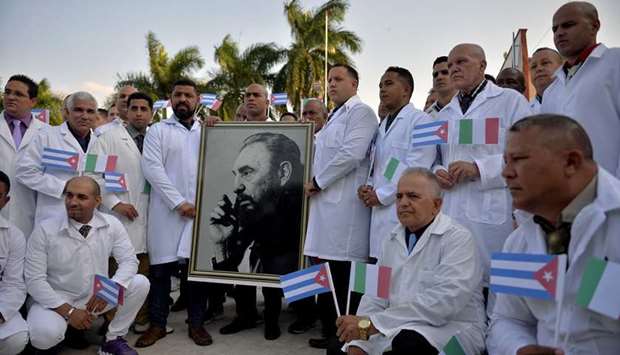Doctors and nurses of Cubau2019s Henry Reeve International Medical Brigade pose with a portrait of late leader Fidel Castro as they are bidding farewell before travelling to Italy to help in the fight against the coronavirus  pandemic, at the Central Unit of Medical Co-operation in Havana.