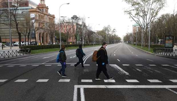 People wearing protective face masks keep social distancing as they cross an almost deserted Paseo de la Castellana street during the coronavirus disease (COVID-19) outbreak, in Madrid Spain