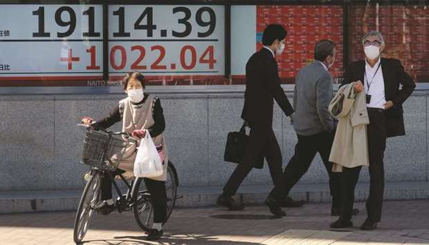 Pedestrians pass in front of a quotation board displaying share price numbers on the Tokyo Stock Exchange in Japan. Tokyo stocks surged over 8% yesterday, in their best percentage gain since 2008, on news of a $2tn coronavirus rescue package and relief that the Tokyo Olympics was postponed, not cancelled.