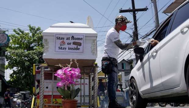 A volunteer (centre) manning a checkpoint flags a vehicle next to a coffin with a note u201cstay at home or stay insideu201d on display to keep residents from going out, in the town of Santo Tomas, Pampanga province, north of Manila yesterday, after the nationu2019s main island of Luzon was put under quarantine due to rising Covid-19 coronavirus cases.