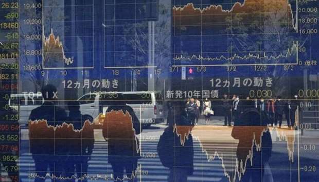 Pedestrians reflected in a window stand in front of a quotation board displaying the numbers on the Tokyo Stock Exchange. The Nikkei index ended down 4.5% at 18,664.60 points yesterday.