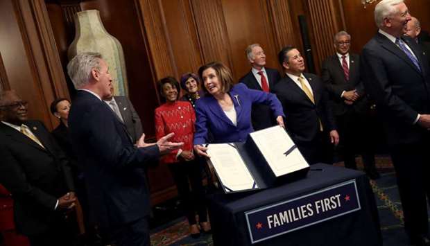 Pelosi surrounded by a bipartisan group of members of the House, shows off the stimulus bill known as the CARES Act after the bill was passed at the US Capitol in Washington, DC. On the left is McCarthy.